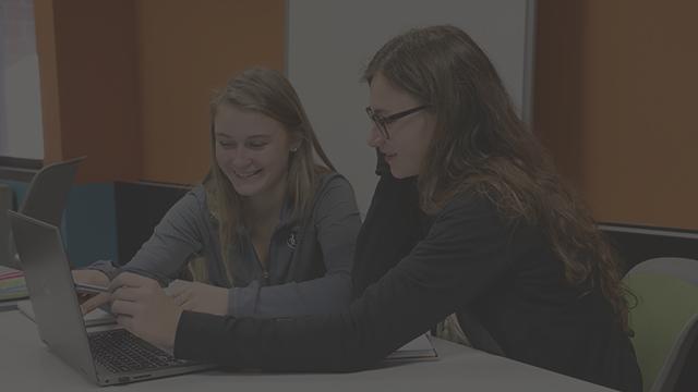 Two women look at a laptop. One is pointing at the screen.